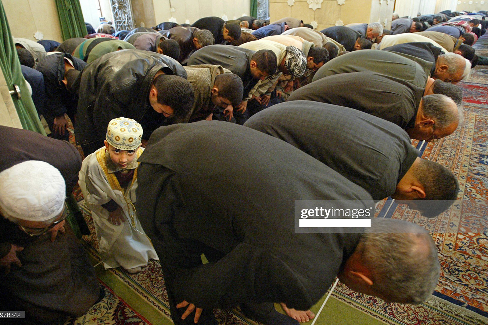 BAGHDAD, IRAQ:  An Iraqi Sunni boy, surrounded by older men, performs the Friday midday prayer at the Abu Hanifa mosque in Baghdad's Sunni neighborhood of Azamiya13 February 2004. The top UN envoy to Iraq, Lakhar Brahimi, said in a meeting with the Iraqi Governing Council that the timing of elections in the war-torn country should not be tied to a specific deadline, but that the timing should flexible to allow for good preparations.  AFP PHOTO/ Daniel MIHAILESCU  (Photo credit should read DANIEL MIHAILESCU/AFP via Getty Images)