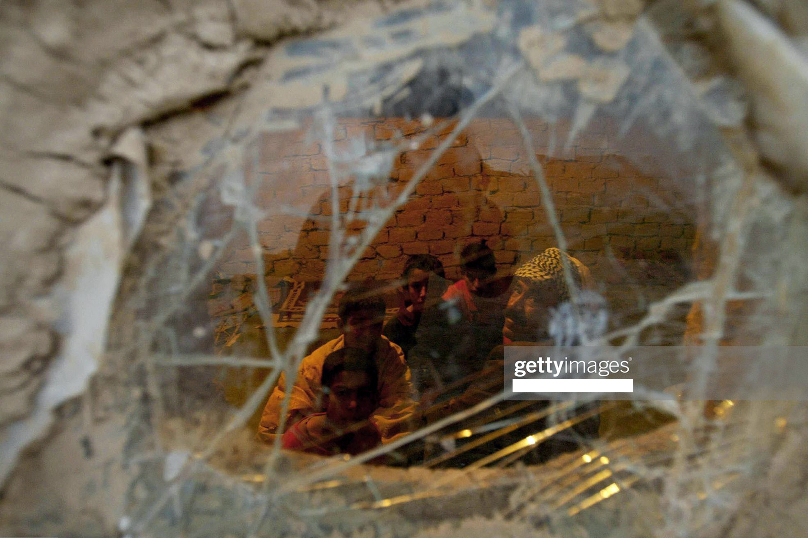 KIRKUK, IRAQ:  An Arab family looks through broken glass window of their mud brick home in Nasiriah Yaychi village, near Kirkuk 17 February 2004. A high-ranking Kurdish official reiterated that the northern oil city of Kirkuk, which was arabised by Saddam Hussein, should be included in the three provinces of Iraqi Kurdistan. AFP PHOTO DANIEL MIHAILESCU  (Photo credit should read DANIEL MIHAILESCU/AFP via Getty Images)