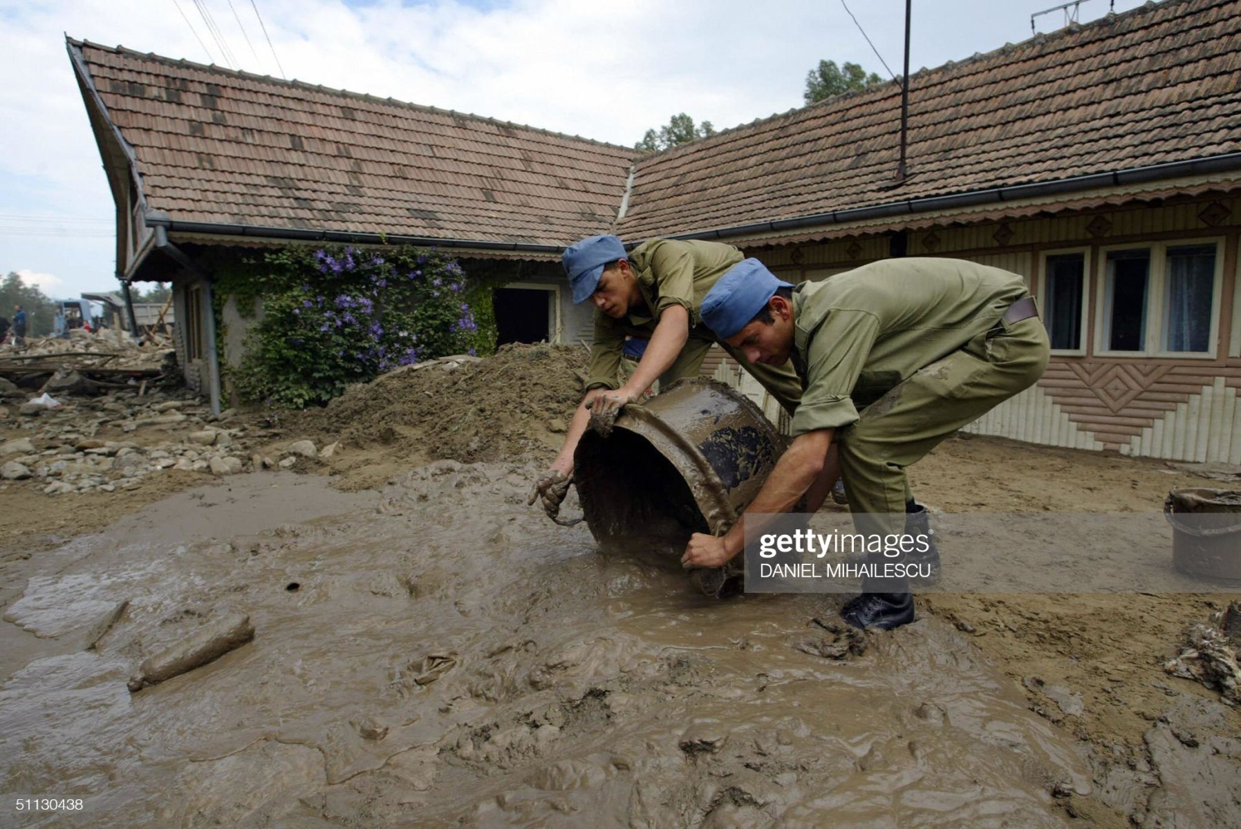 BACAU, ROMANIA:  Romanian soldiers start the clearing up process by carrying mud from inside a house in the village of Agas some 300 km west of Bucharest, 30 July 2004. Three people were killed and about 2,000 left stranded by major flooding that cut off roads and railway lines in northern and central Romania, the environment ministry said Thursday. Officials said about 50 bridges and numerous dams were destroyed by the floods, as waters continued to rise. They said more than 2,000 houses were damaged and thousands of residents deprived of electricity.  AFP PHOTO DANIEL MIHAILESCU  (Photo credit should read DANIEL MIHAILESCU/AFP via Getty Images)