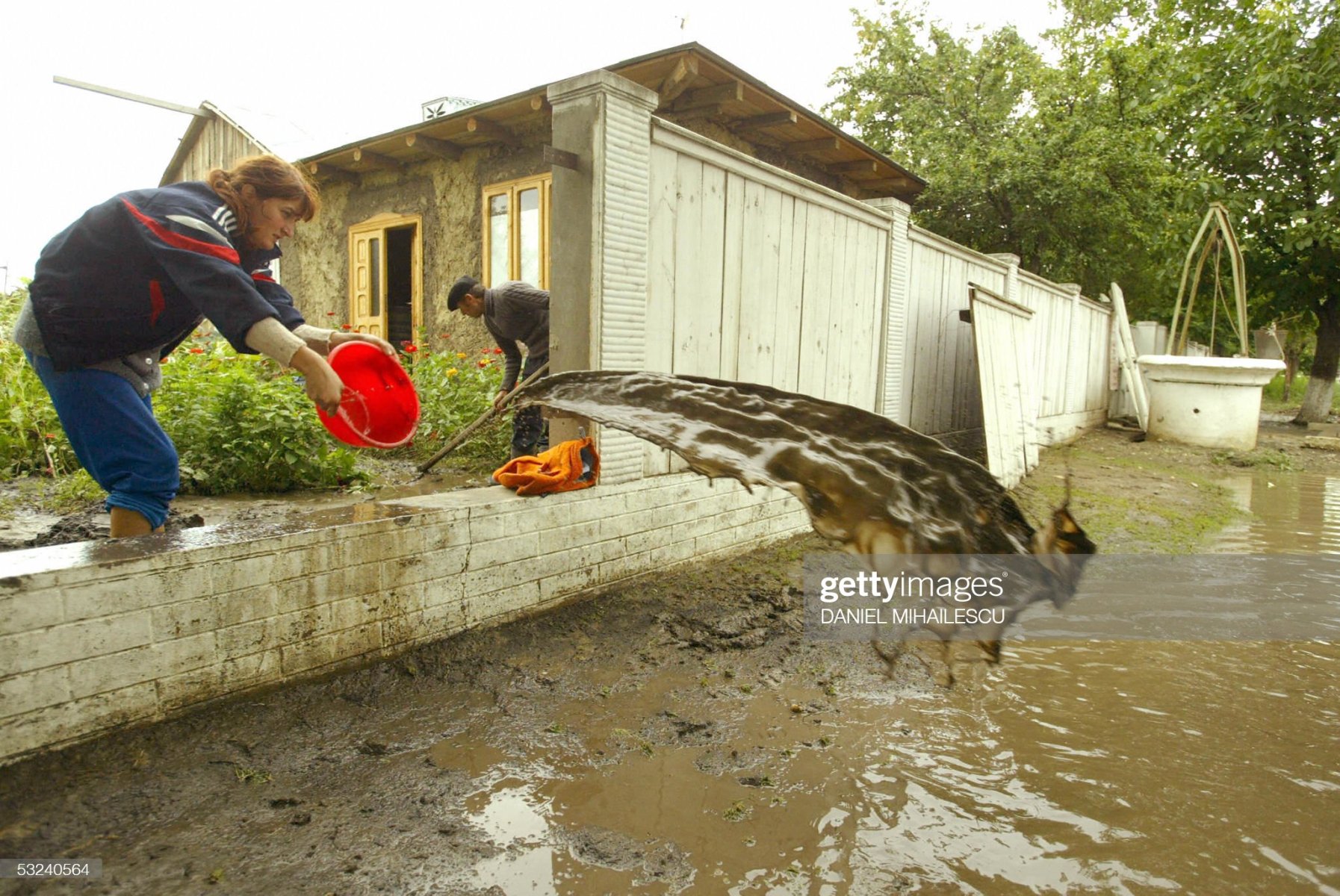 FUNDENI, ROMANIA:  A villager throuts out water from her flooded courtyard after a flash flood caused by Siret river in Fundeni village, 300 kms north-east from Bucharest, 15 July 2005. Seven people were killed and seven are missing after severe flooding in Romania that has affected 30 of the countries 42 regions, authorities said 13 July. An estimated 210,000 hectares (500,000 acres) of crops have also been damaged at a cost of 500 million euros (600 million dollars), according to government estimates. The flooding began on Tuesday after two weeks of heavy rains and has inundated thousands of homes and cut roads and railway lines, blocking traffic in several regions. Press reports said the floods, which have damaged thousands of homes and dozens of bridges, roads and railway lines, were the worst in the country for 30 years. AFP PHOTO DANIEL MIHAILESCU  (Photo credit should read DANIEL MIHAILESCU/AFP via Getty Images)